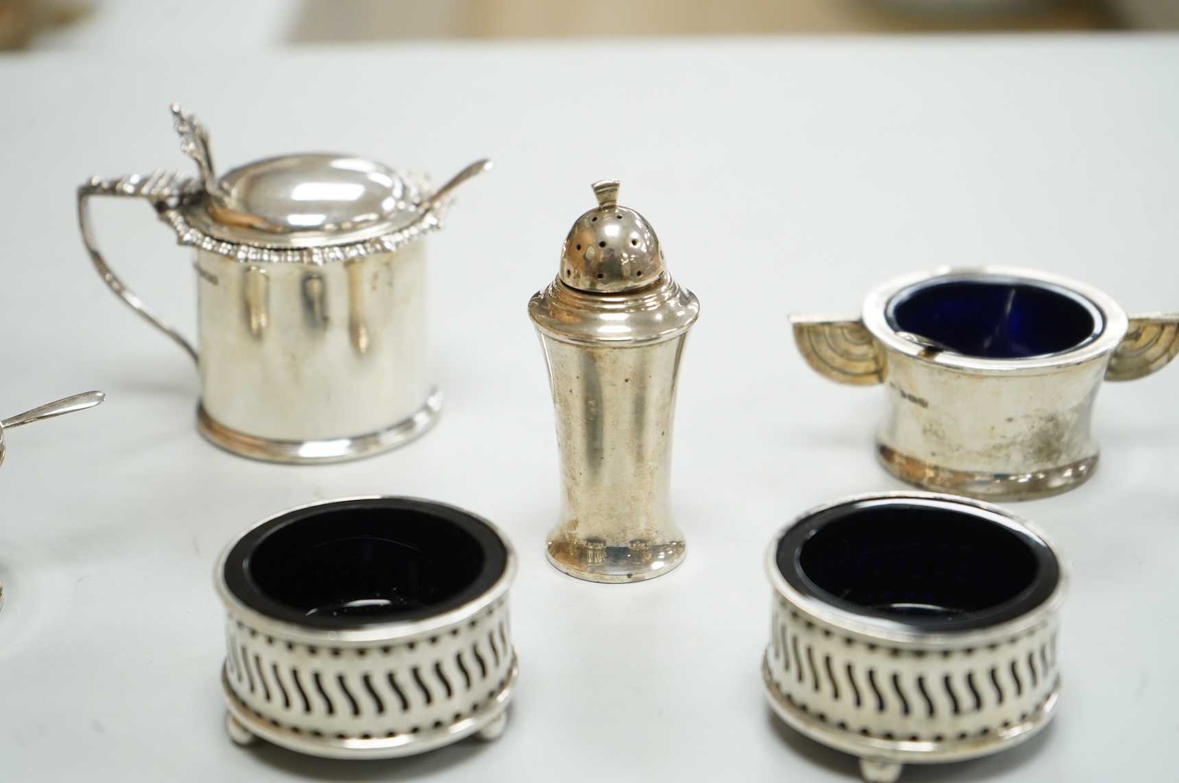 A George V Art Deco three piece silver condiment set and two spoons by William Adams Ltd, Birmingham, 1935, together with a pair of late Victorian pierced silver salts with blue glass liners and an Edwardian silver musta